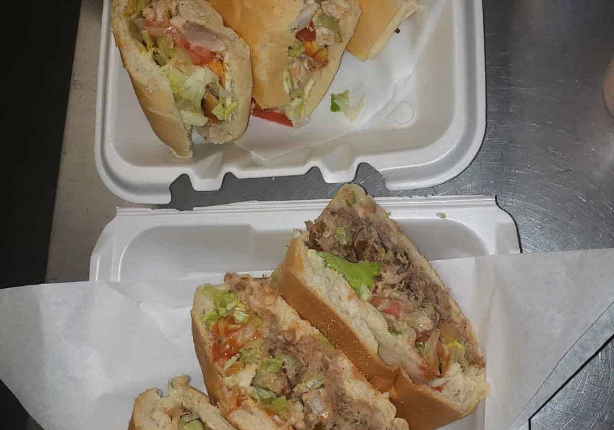 Four Halves Of Stuffed Submarine Sandwiches In Takeout Containers.